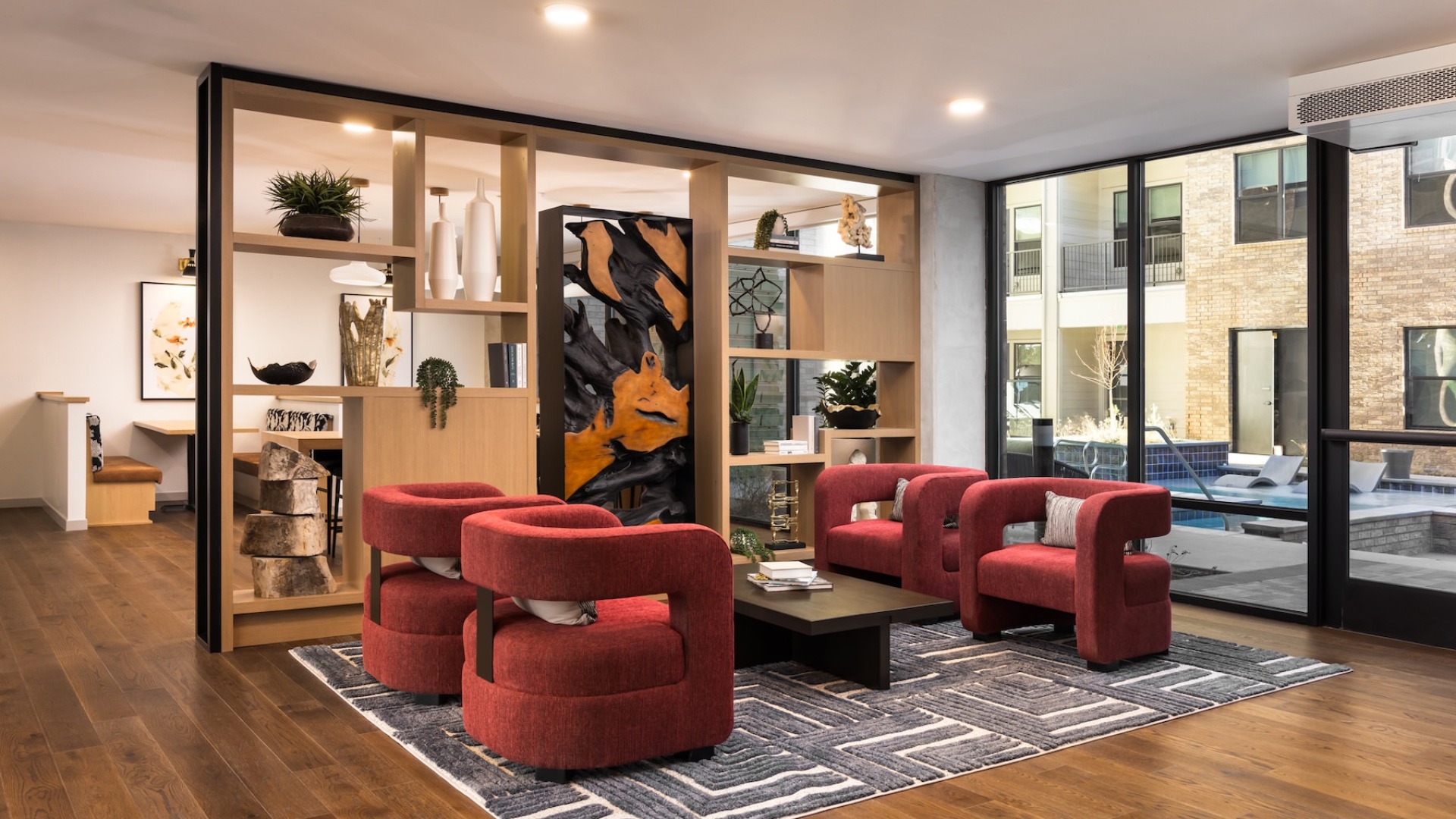 a room with red chairs and a coffee table next to a shelf with decorations