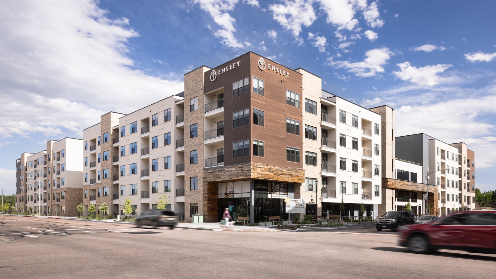 exterior of a multi-story building at a street corner with cars driving down the street